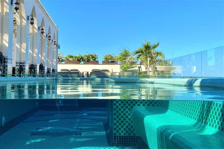 Indoor lap pool with underwater viewing window, architectural columns, and palm trees