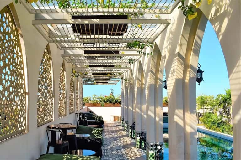 Covered pergola walkway with geometric lattice panels, seating area, and pool view beyond