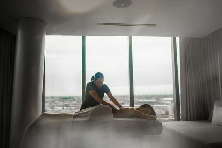 Massage therapist performing treatment on client in high-rise spa room with city skyline view