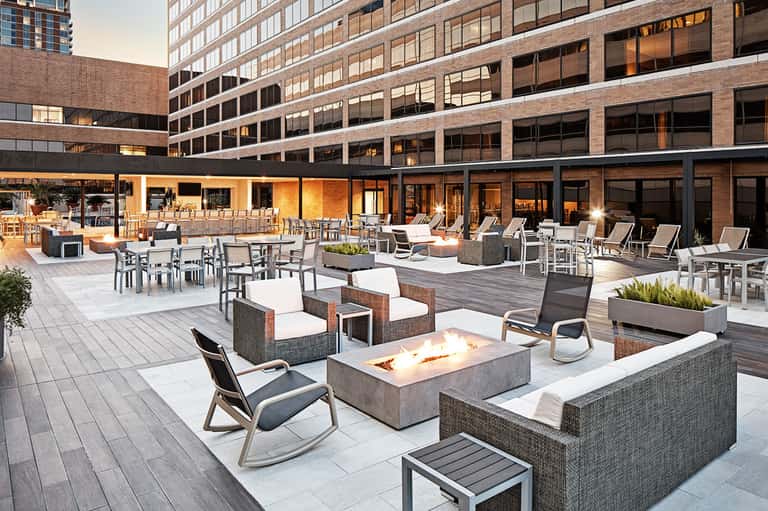 Upscale rooftop terrace with fire pit, lounge seating, and modern high-rise buildings at dusk