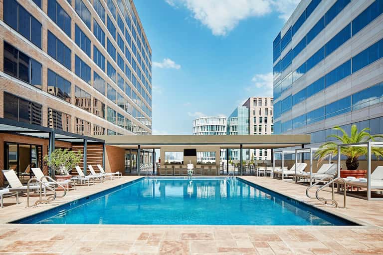 Luxury rooftop pool surrounded by high-rise buildings with lounge chairs and palm trees