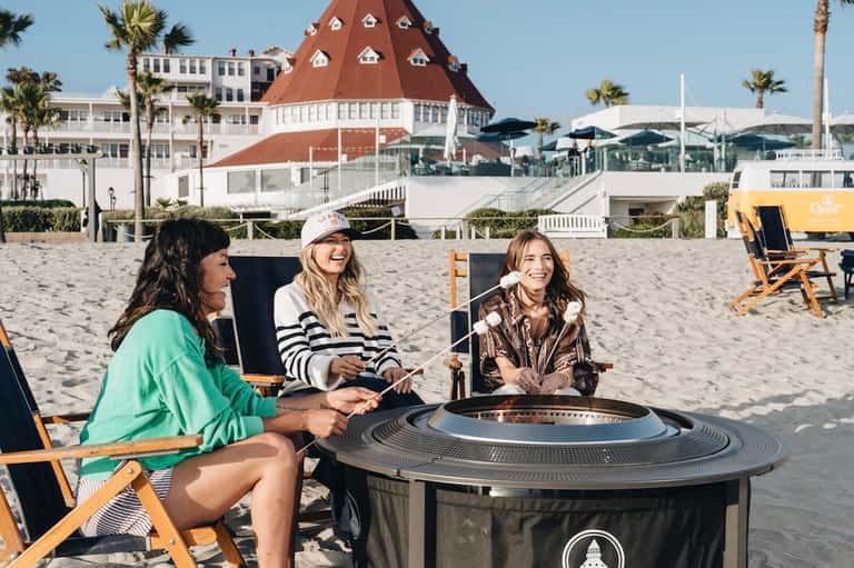 Beachfront guests gathering by fire pit near iconic red-roofed historic building and ocean