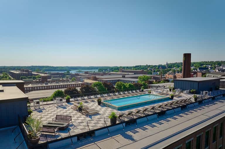 Rooftop swimming pool with blue water overlooking industrial cityscape and distant waterfront
