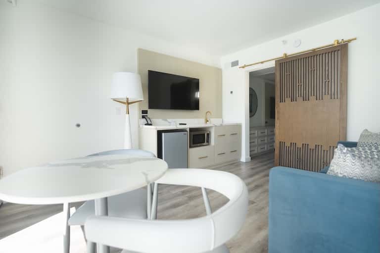 Modern hotel suite with TV, kitchenette, seating area, and wooden barn doors