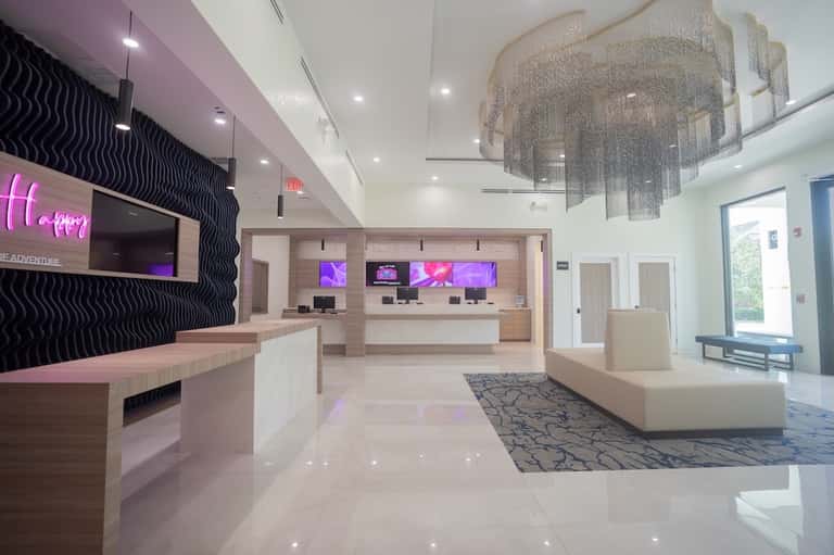 Modern hotel lobby with pink neon signage, reception desk, and contemporary light fixture