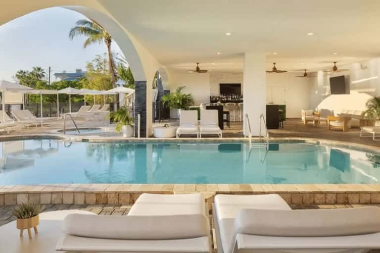 Indoor pool facility with arched architecture, lounge chairs, and palm plants