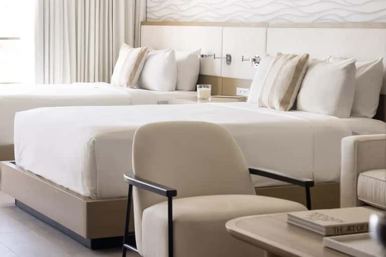 Luxury hotel suite with two queen beds, cream bedding, accent chair, and contemporary decor