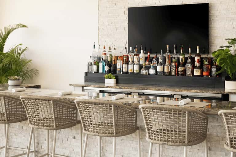 Modern outdoor bar with white wicker stools, extensive liquor selection, and minimalist design