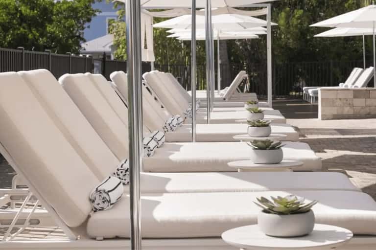 Outdoor spa lounge with white cushioned loungers, rolled towels, succulents, umbrellas, and pergola pergola seating area