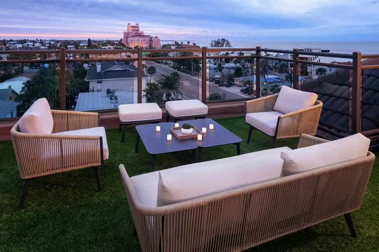 Rooftop lounge with wicker furniture, pink cushions, and city skyline at dusk