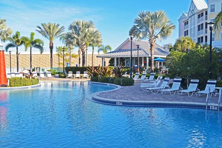 Resort pool surrounded by palm trees, lounge chairs, tropical vegetation, and white gazebo