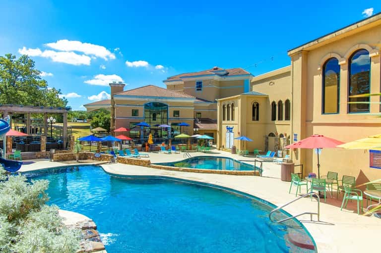 Resort pool complex with blue water, colorful umbrellas, architectural buildings, and landscaping