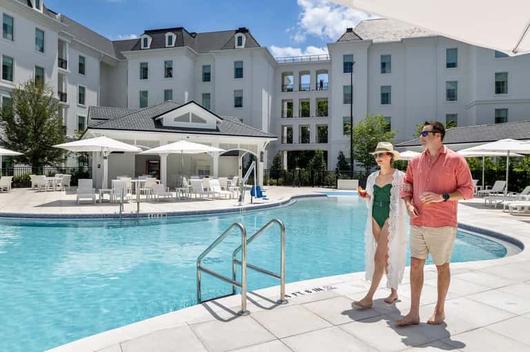 Couple walking alongside large resort pool with white umbrellas and elegant architecture