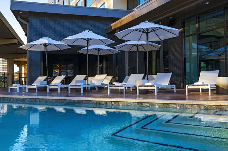Contemporary resort pool with lap lane, lounge chairs, blue umbrellas, and modern building