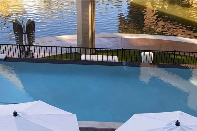 Indoor pool with waterfront view, black railing, white lounge chairs, and reflected water scenery
