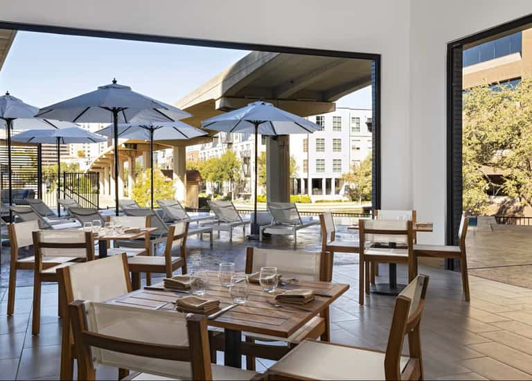 Contemporary terrace dining area with wooden tables, canvas umbrellas, lounge chairs, and urban city views