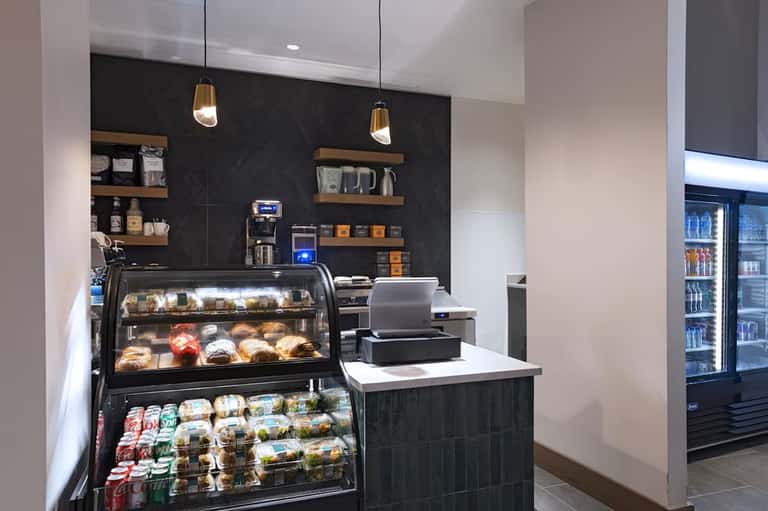 Contemporary café counter with pastry display case, espresso machine, shelving, and beverage refrigerators