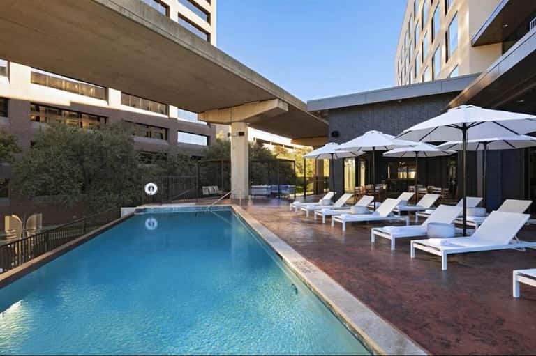 Contemporary urban pool deck with white lounge chairs, umbrellas, and modern building architecture