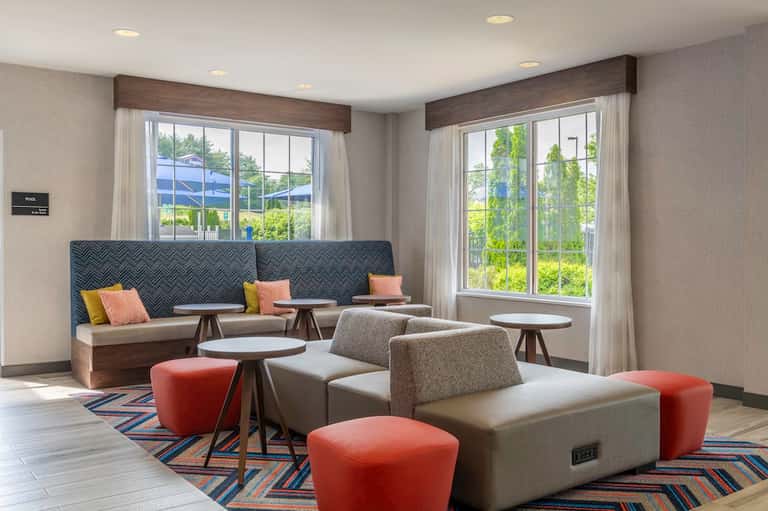 Modern lounge with patterned banquette seating, side tables, colorful pillows, and floor-to-ceiling windows