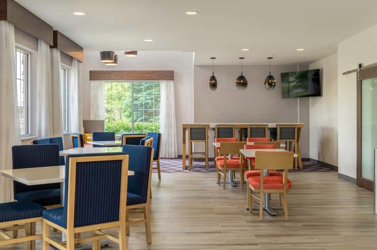 Modern hotel gathering space with navy chairs, natural lighting, TV, and outdoor access