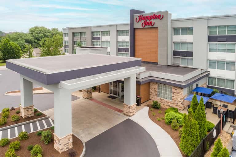 Modern Hampton Inn hotel exterior with covered entrance and outdoor seating area