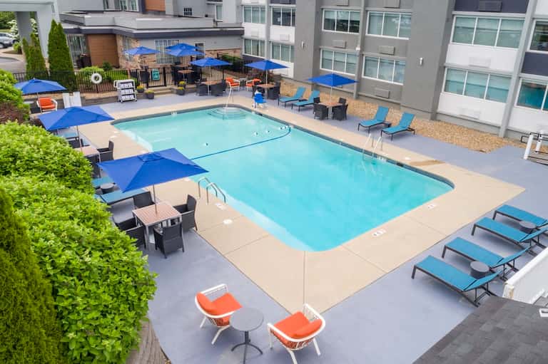 Residential pool area with blue umbrellas, loungers, and multi-story apartment buildings nearby