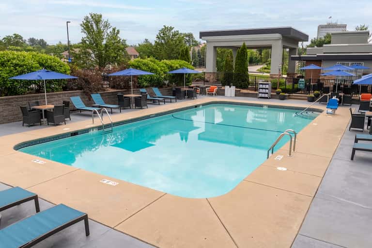 Modern resort pool with sun loungers, blue umbrellas, shade structures, and landscaping