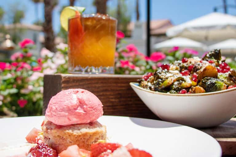 Outdoor dining area with pink ice cream dessert, tropical cocktail, and flowering garden in sunny setting
