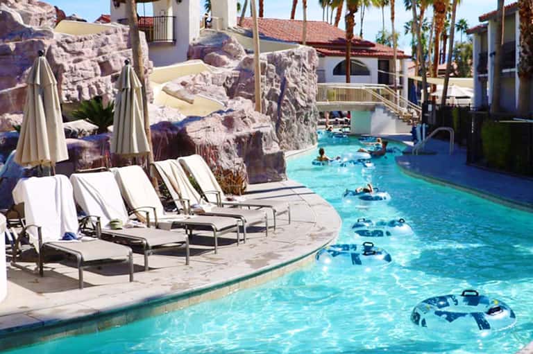 Resort pool with turquoise water, white lounge chairs with umbrellas, and artificial rock formations