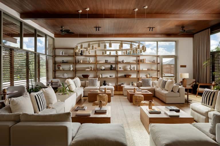 Luxury living room with wooden beamed ceiling, shelving, cream seating, and large windows