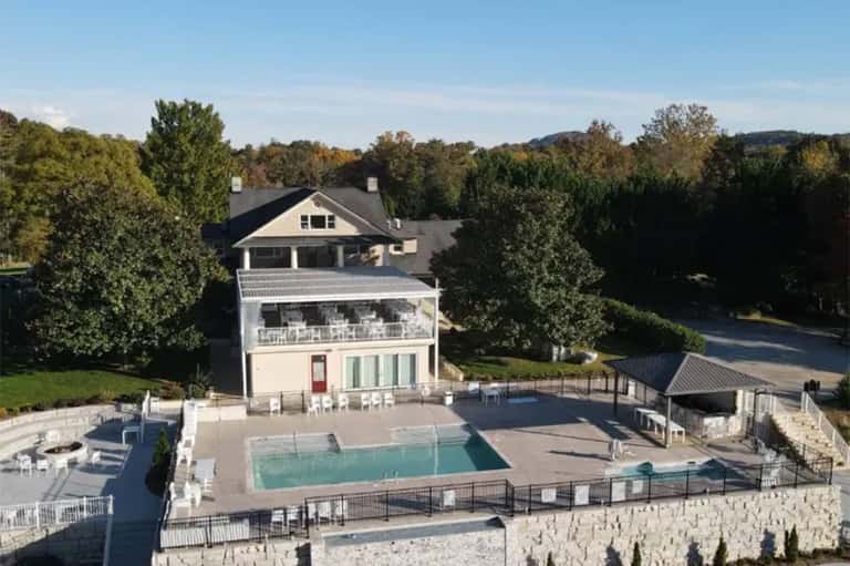 Aerial view of luxury home with pool, multi-level deck, and mature landscaping on wooded property