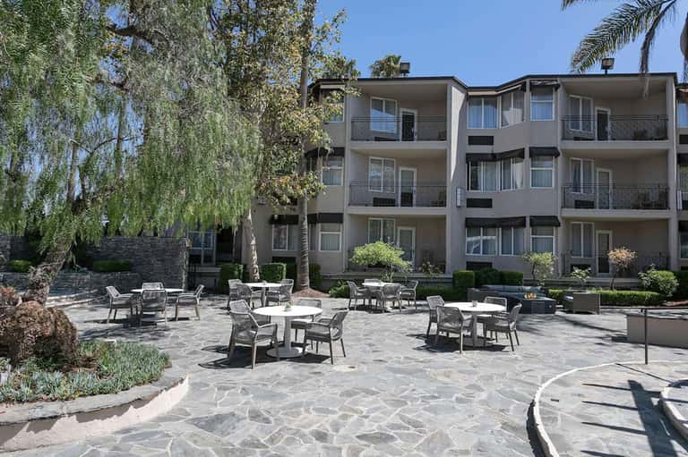 Resort courtyard with casual seating area, stone patio, landscaping, and multi-story building