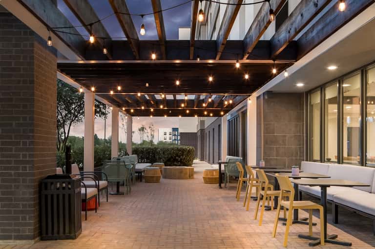 Modern covered patio with hanging lights, seating areas, and contemporary architecture at dusk