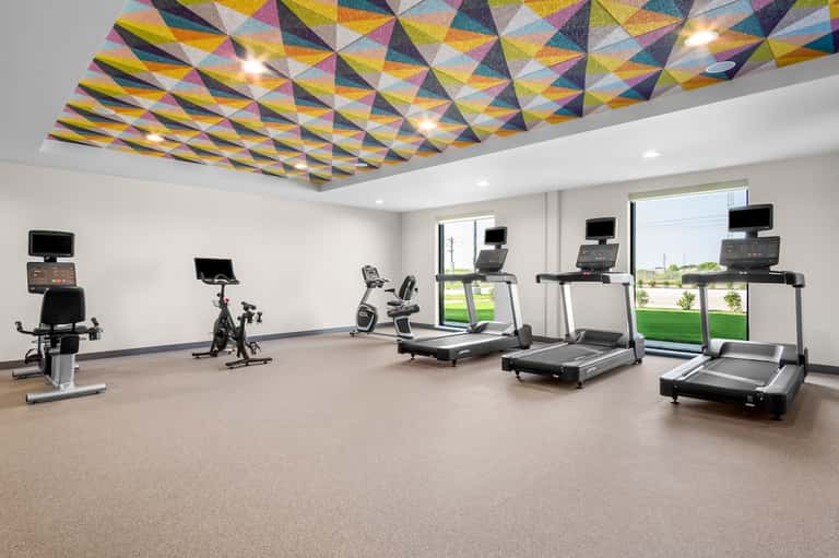 Contemporary fitness room with geometric ceiling design, treadmills, exercise bikes, and large windows