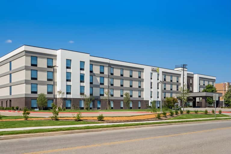 Modern hotel building with cream and brown facade, manicured landscape, and clear blue sky