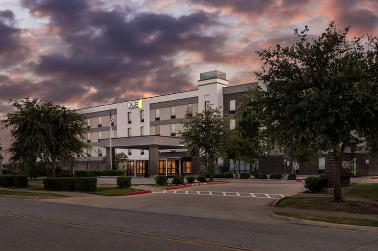 Home2 hotel exterior at dusk with illuminated entrance, landscaping, and modern architecture