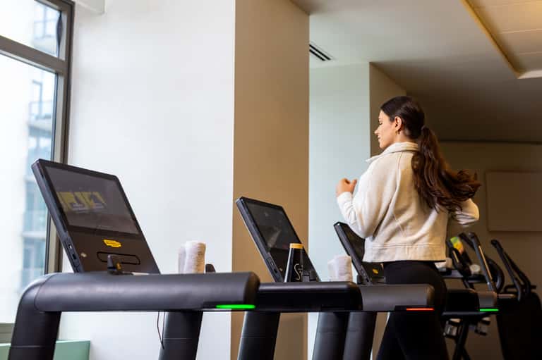 Woman exercising on treadmill in bright modern gym with large windows and contemporary equipment