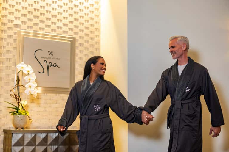 Spa staff members in black robes walking past Waldorf Astoria Spa entrance with orchid flowers