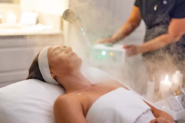 Spa treatment room with woman receiving facial therapy and lit candles in bathroom setting