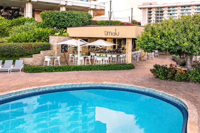 Poolside restaurant terrace with white umbrellas, dining tables, and lush greenery