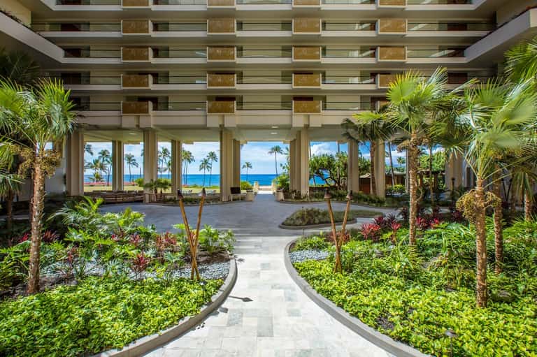 Resort atrium lobby with tall columns, tropical plants, and ocean views through tall windows