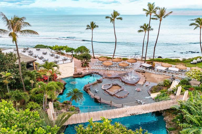 Beachfront resort pool complex with hot tubs, palm trees, ocean views, and multiple lounge areas