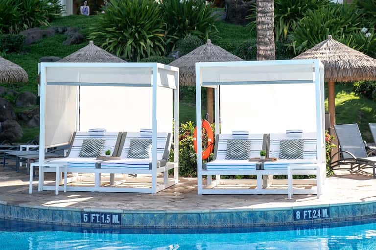 Poolside white canopy cabanas with adjustable curtains overlooking water depth markers