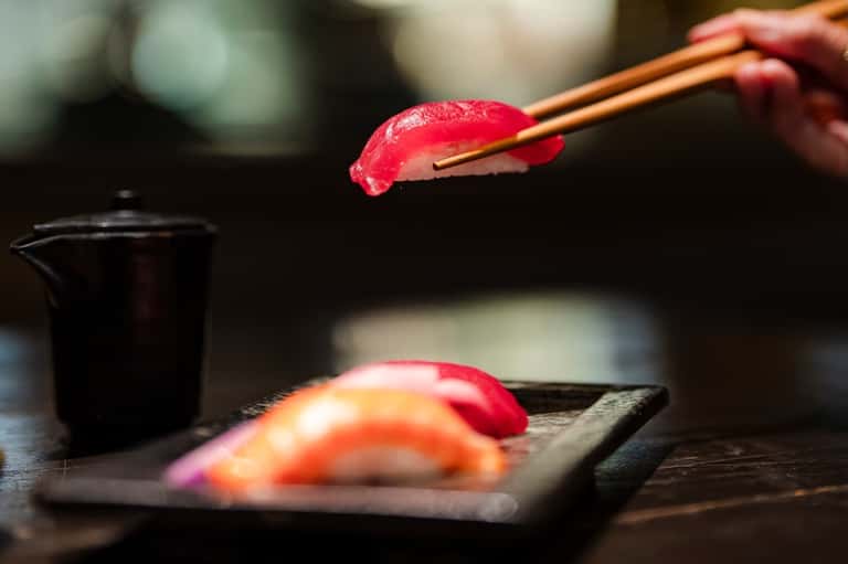 Close-up of fresh sushi being held with chopsticks over a black serving plate