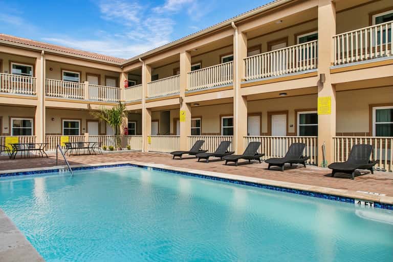 Courtyard-style pool area with multi-story beige hotel building and lounge chairs