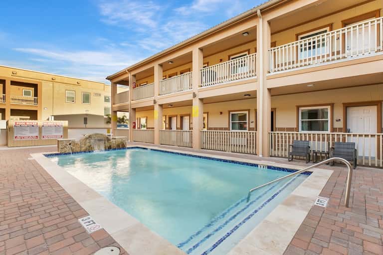 Hotel courtyard pool with turquoise water, multi-story building with balconies, and lounge seating