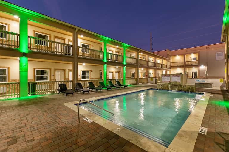 Outdoor pool at night with green-lit pillars, chaise lounges, and illuminated hotel building