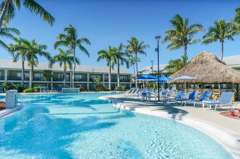 Large lagoon-style pool with palms, tiki umbrellas, lounge chairs, tropical resort setting