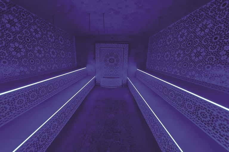 Purple-lit hammam spa corridor with ornate Moroccan tilework and glowing neon accent lighting