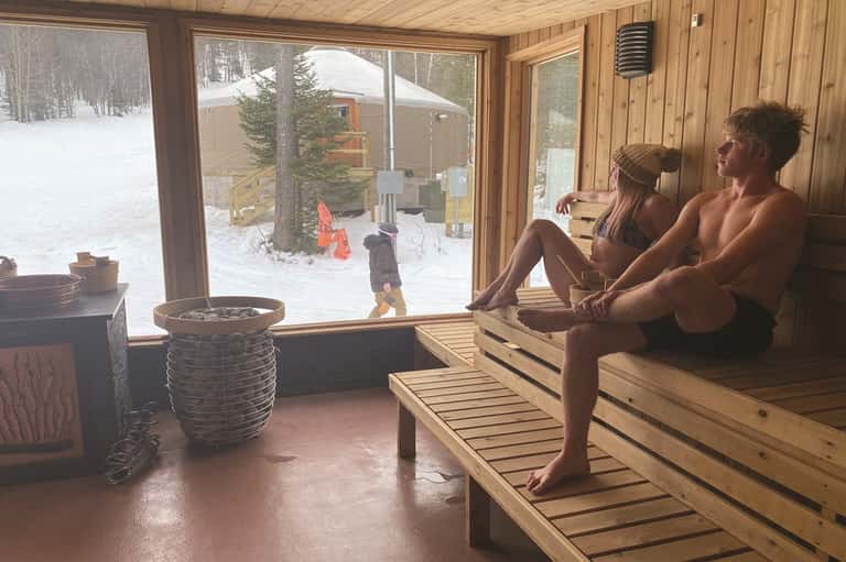 Sauna interior with wooden benches and large windows overlooking snowy winter landscape